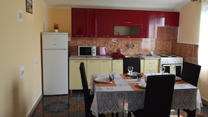 Une cuisine compacte avec des meubles rouges, un réfrigérateur blanc, un four à micro-ondes, une cuisinière et une table à manger pour deux personnes.