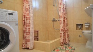 Une salle de bain équipée d’un lave-linge, d’une douche, de toilettes et d’un petit tabouret en bois.