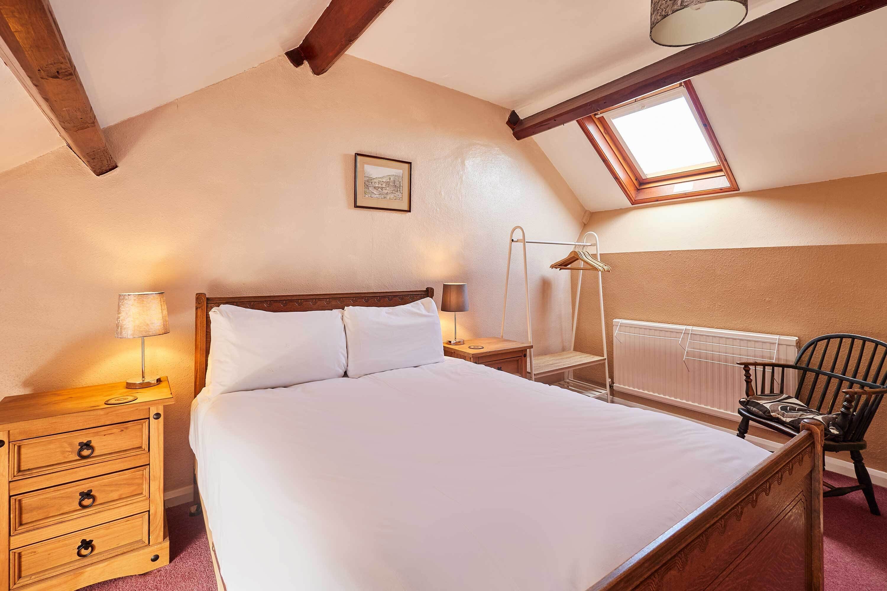 Ein Schlafzimmer mit einem Holzbett, Nachttischen, einer Lampe, einem Sessel, einer Heizung und einem Oberlicht.