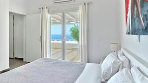 Een hotelkamer met een bed, witte gordijnen, een airconditioning en uitzicht op zee.