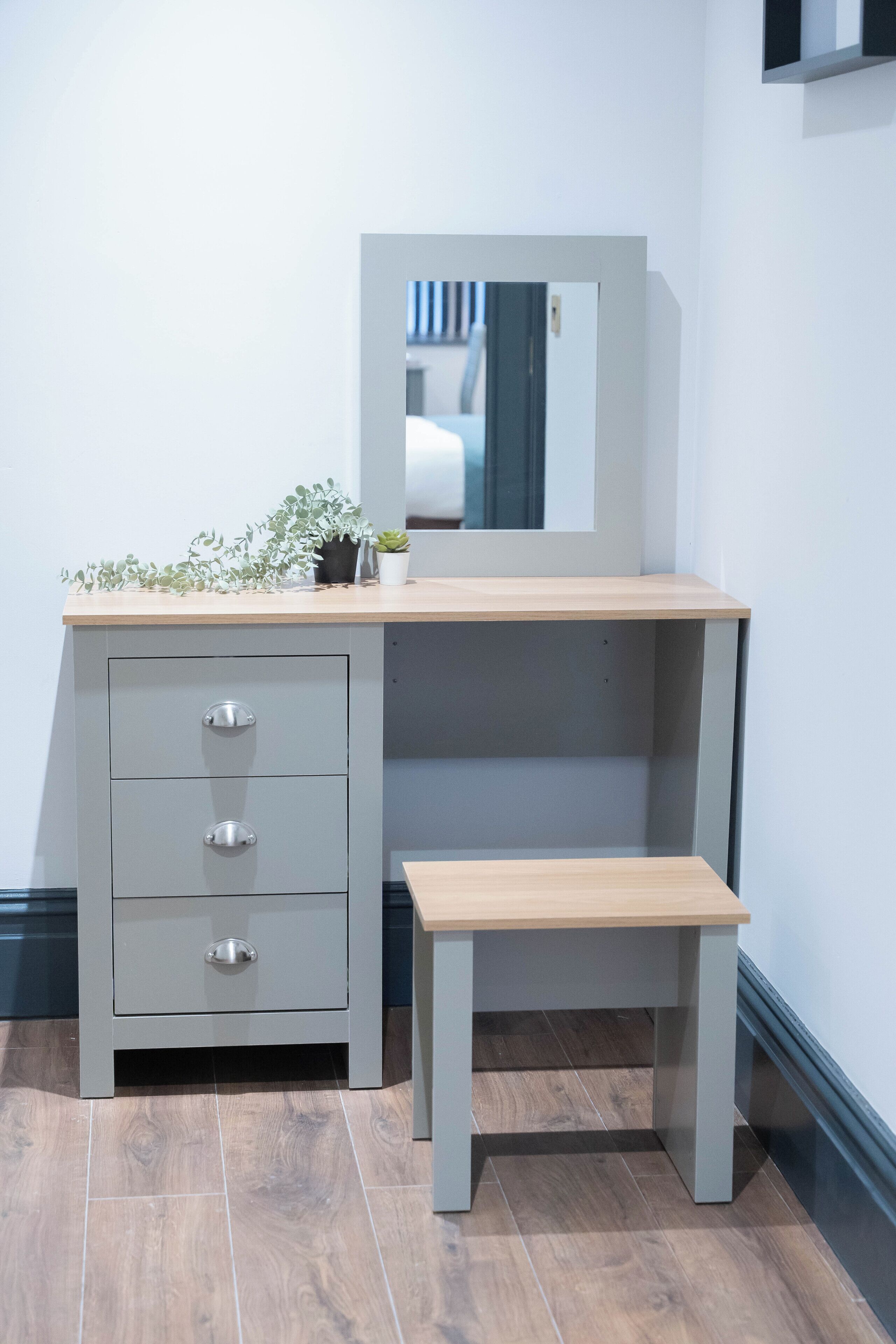 A grey dresser with drawers and a mirror, a small bench, and a potted plant on top.