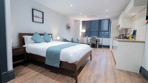 Quarto de hotel moderno com cama de madeira, escrivaninha e cozinha compacta.