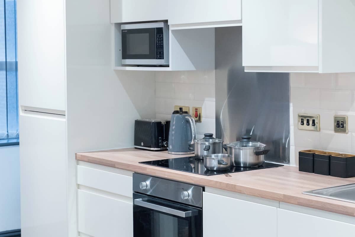 Egy modern konyha fehér szekrényekkel, mikrohullámú sütővel, pirítóval, vízforralóval és sütővel.