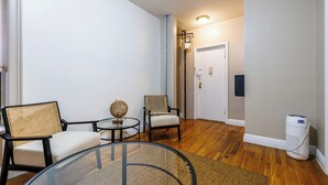 A room with a glass table, two chairs, a small round table with a globe, a standing heater, and a door in the background. - Centrally Located 2Bedroom UWS Apartments (New York)