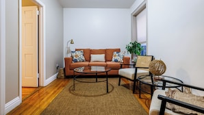 A living room with a sofa, coffee table, and chairs, a door, and a window with blinds. - Centrally Located 2Bedroom UWS Apartments (New York)