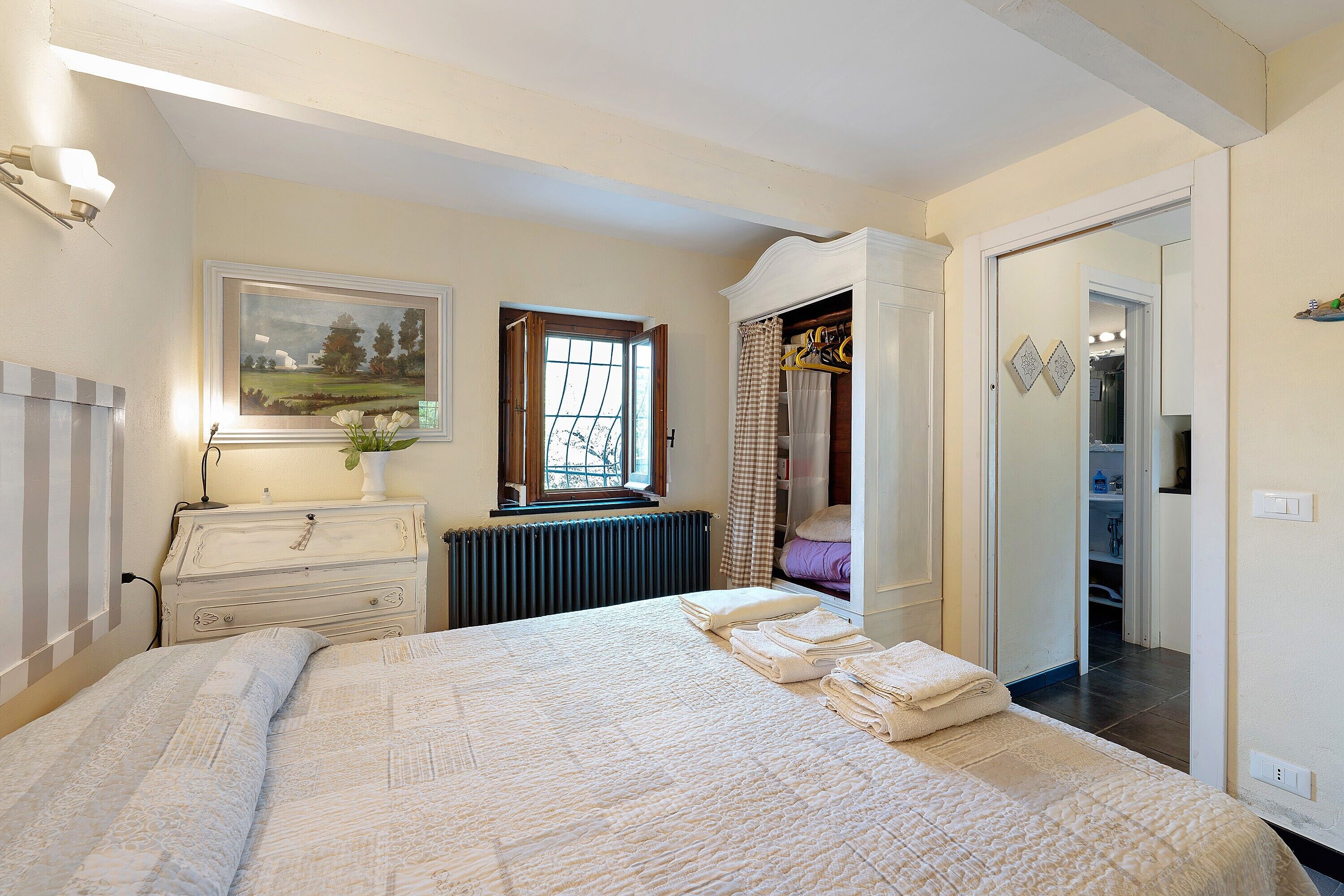A bedroom with a bed, dresser, radiator, and a window with curtains.