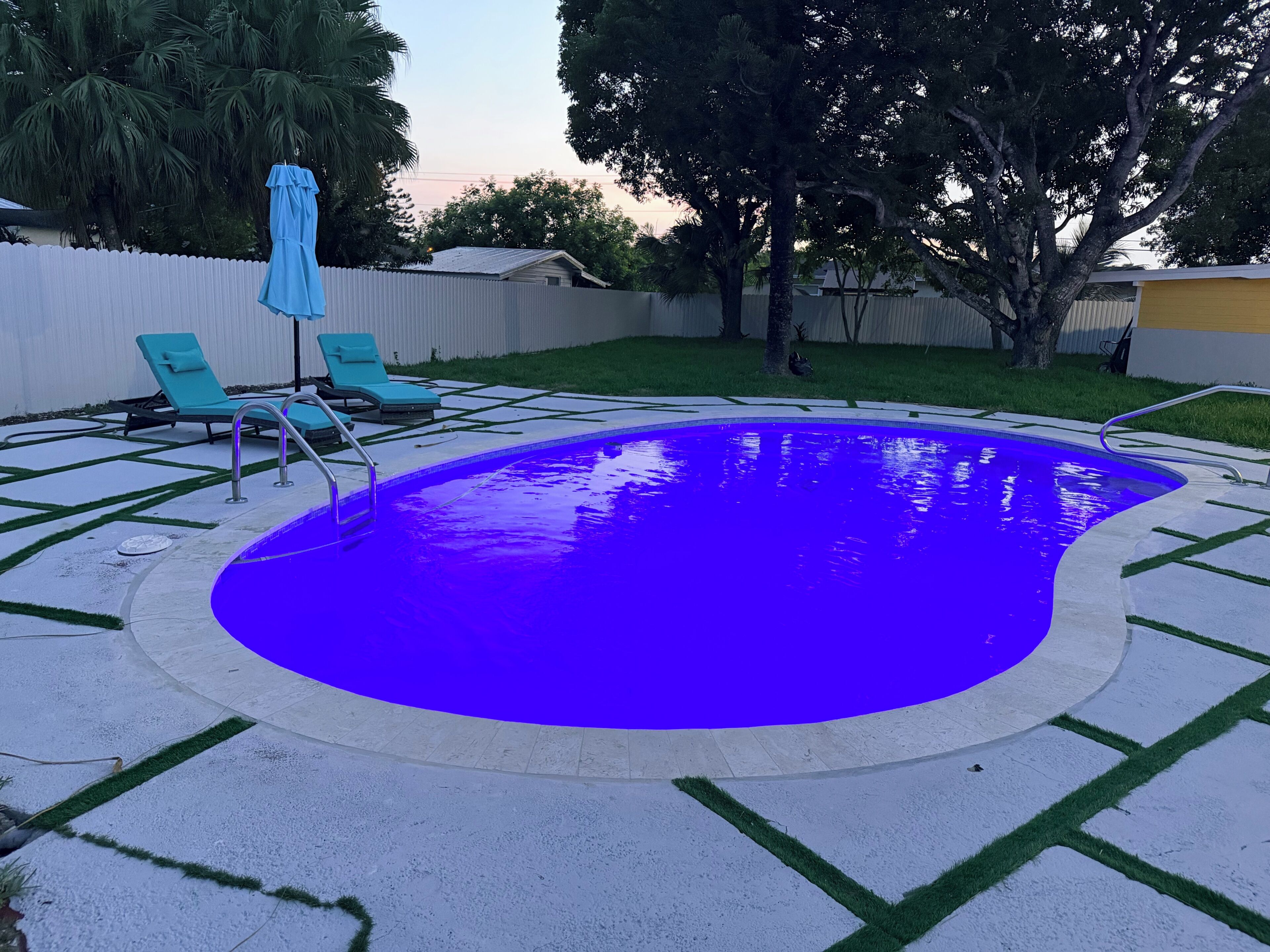 A backyard with a swimming pool, green lawn, and a white fence.