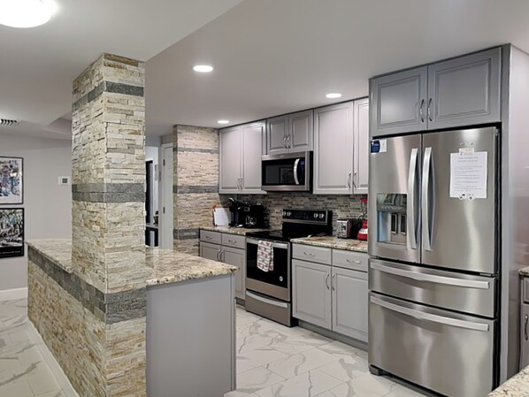 A modern kitchen with granite countertops, stainless steel appliances, and a stone accent wall.