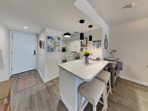A modern kitchen with a central island, pendant lighting, and a view into the dining area.