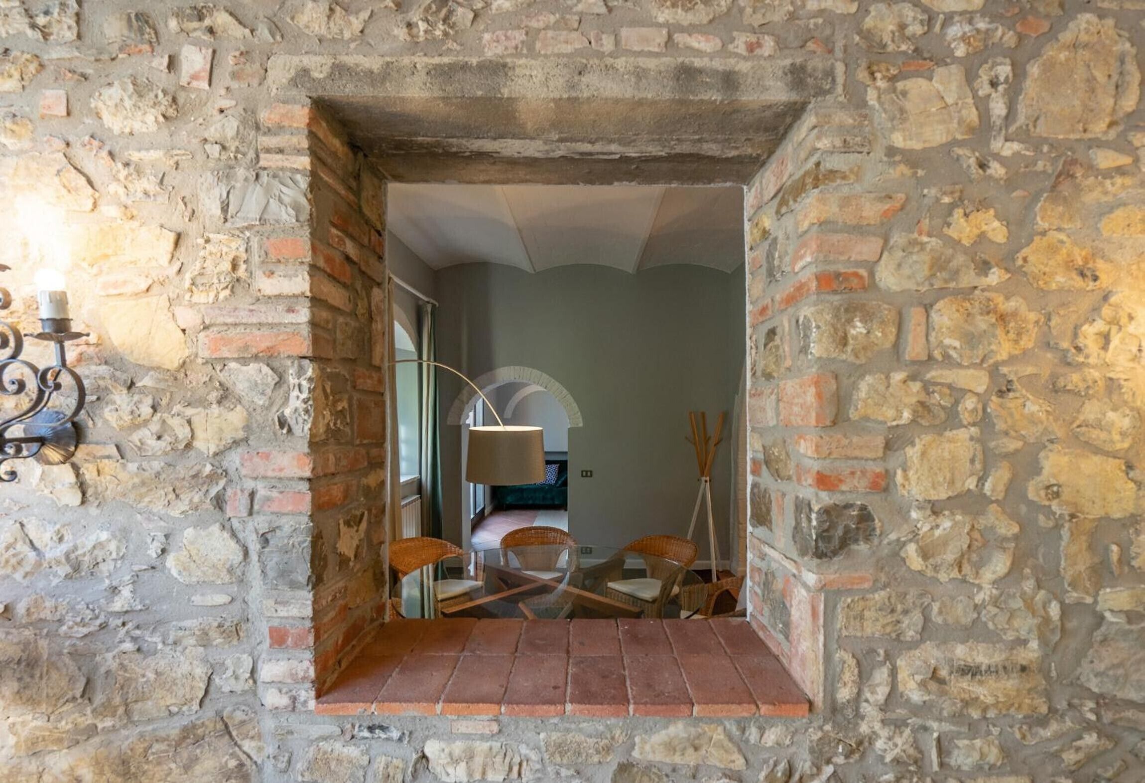 A stone-walled room with a small seating area, a lamp, and a view into another room.