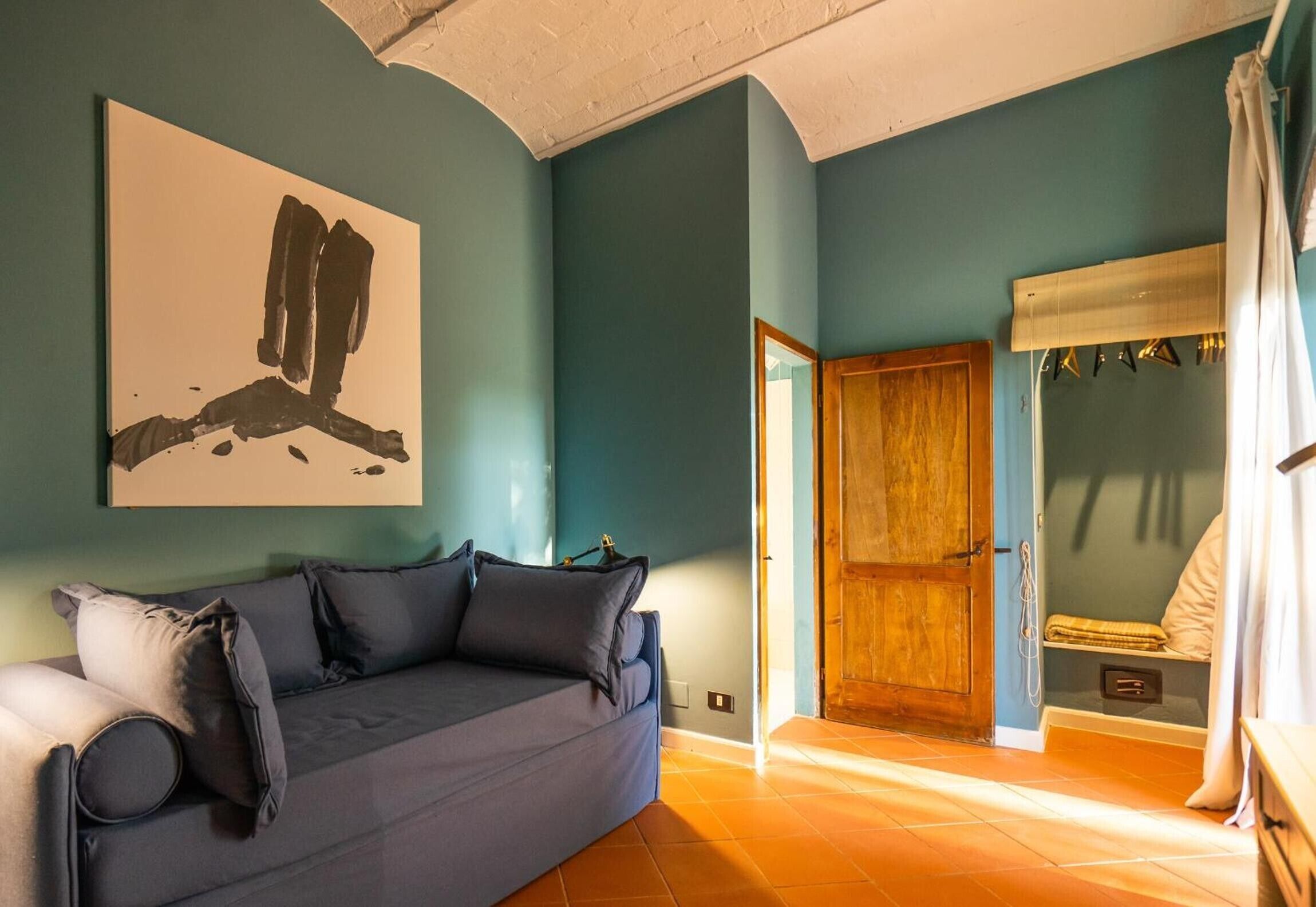 Una habitación con pared azul, puerta de madera, sofá con cojines y un cuadro abstracto de gran tamaño.