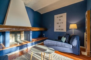 Ein modernes Wohnzimmer mit blauer Wand, einer Couch, zwei kleinen Tischen, einem Kamin und einem Willkommen-Schild.