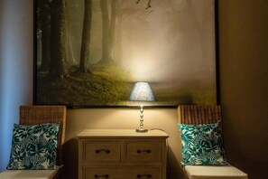 A nightstand with drawers, a lamp, and two chairs with patterned cushions.