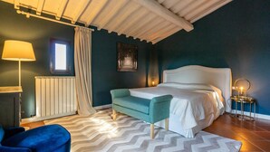 Ein Schlafzimmer mit Bett, einer Bank, einer Lampe, einem Heizkörper, einem Fenster und einem Bild an der Wand.