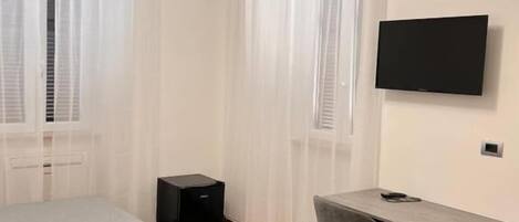 Un dormitorio con cama, escritorio, silla, televisor y altavoz.