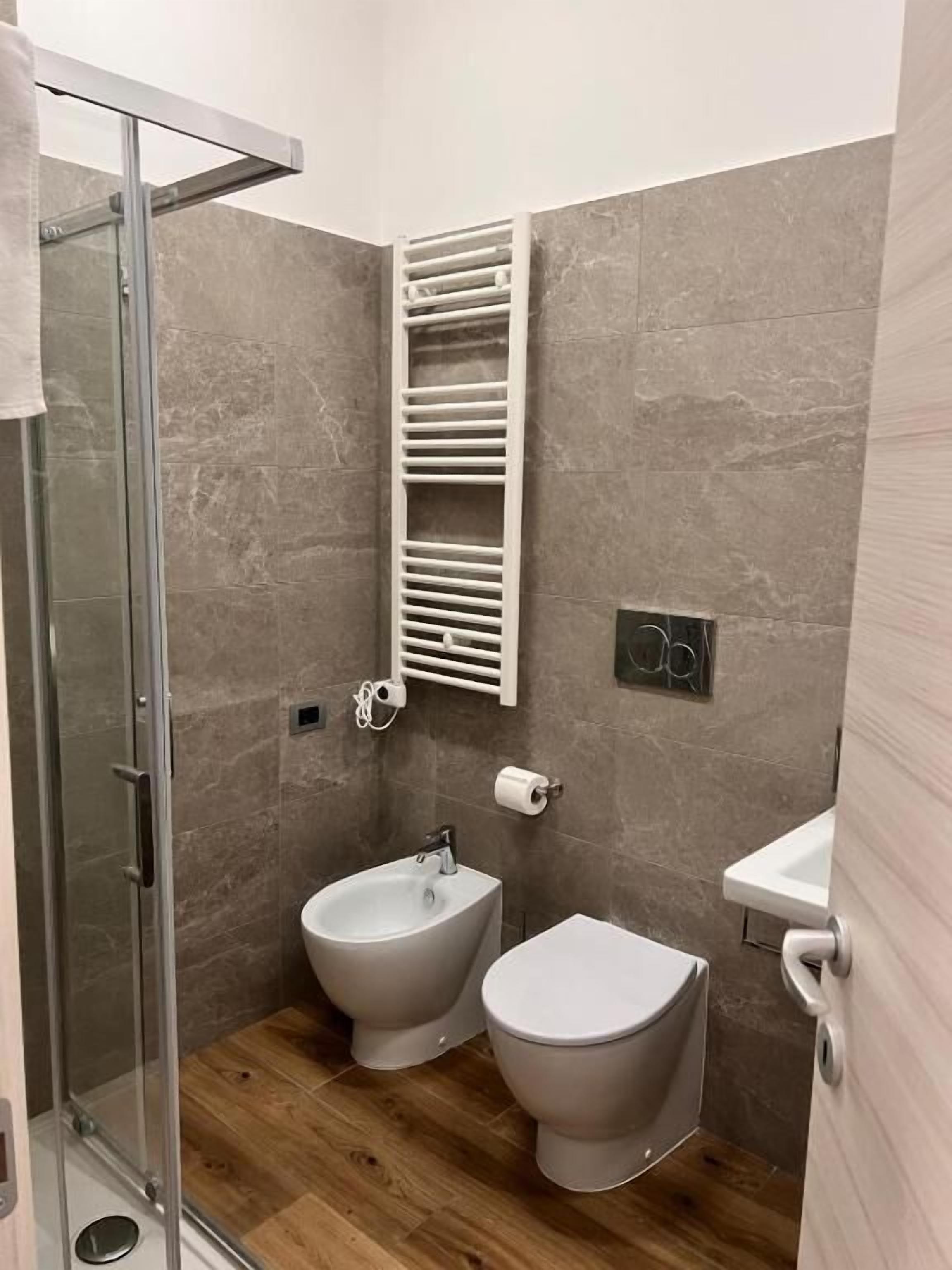 A modern bathroom with a glass shower enclosure, a bidet, a toilet, and a towel rack.