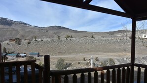 Blick von einer überdachten Veranda auf eine gebirgige Landschaft mit Gebäuden und klarem Himmel.