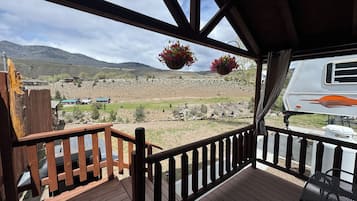 A wooden deck with a railing, a hanging flower basket, and a view of a rural landscape with mountains and houses.
