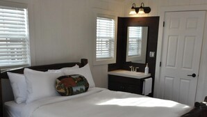Ein Schlafzimmer mit einem hölzernen Bett, weißer Bettwäsche, einem Nachttisch, einem Spiegel und einem Fenster mit Jalousien.