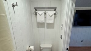 Ein kleines Badezimmer mit weißen Wänden, einer Toilette, einem Handtuchhalter und einem Papierkorb.