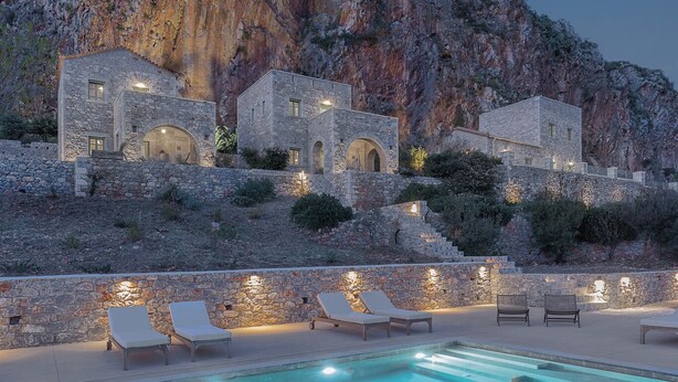 A pool with lounge chairs, stone buildings, and a mountainous backdrop. - Alkyon Seaside Studios (East Mani)