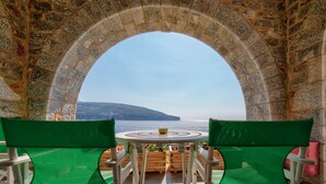 A table with two green chairs facing a stone archway overlooking a body of water. - Alkyon Seaside Studios (East Mani)