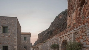 A stone-paved courtyard with buildings, potted plants, and a mountainous backdrop. - Alkyon Seaside Studios (East Mani)