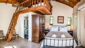 A bedroom with a large bed, a wooden staircase, and a wardrobe. - Alkyon Seaside Studios (East Mani)