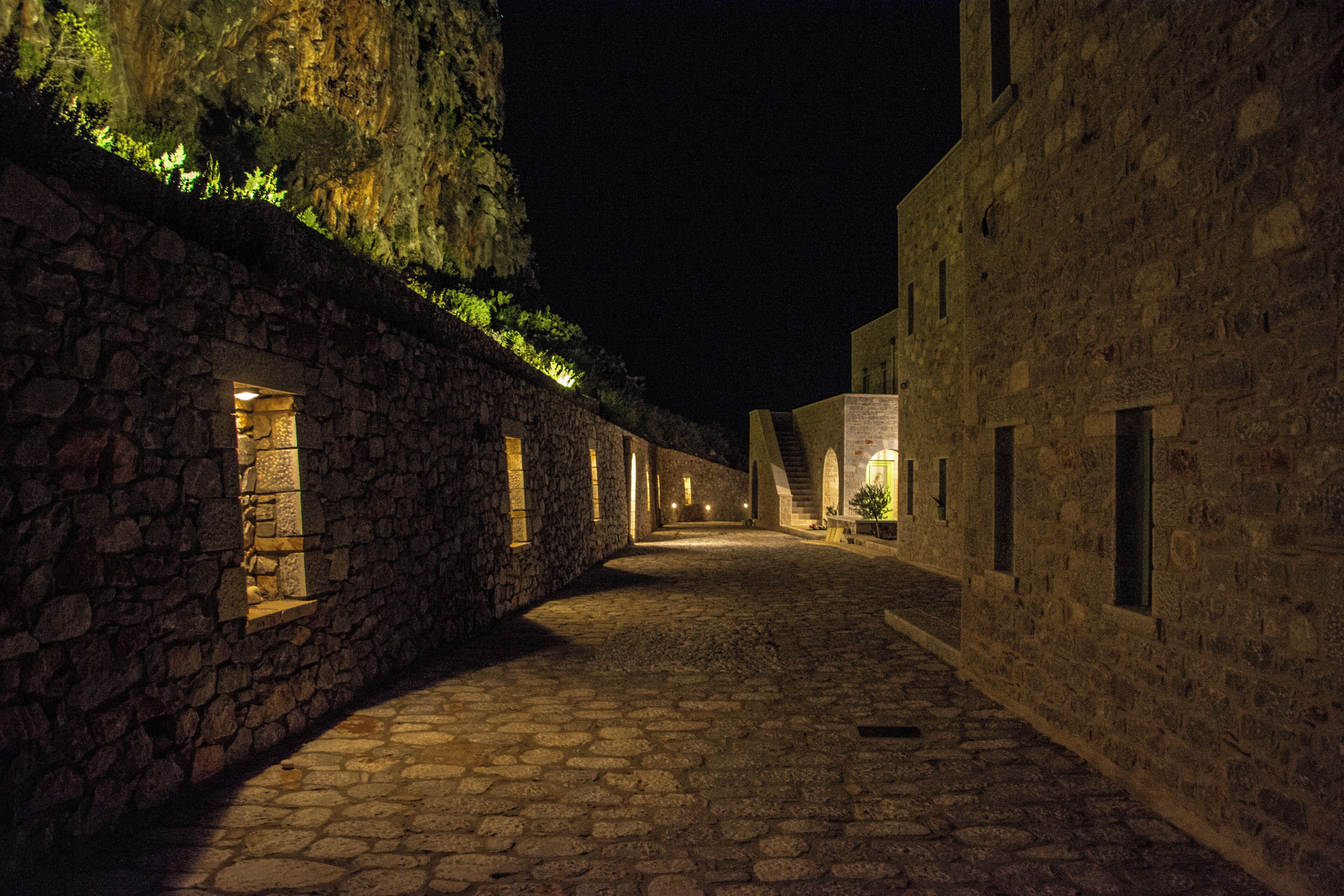 Une ruelle pavée de pierres, bordée de bâtiments des deux côtés, et éclairée par une lumière chaleureuse.