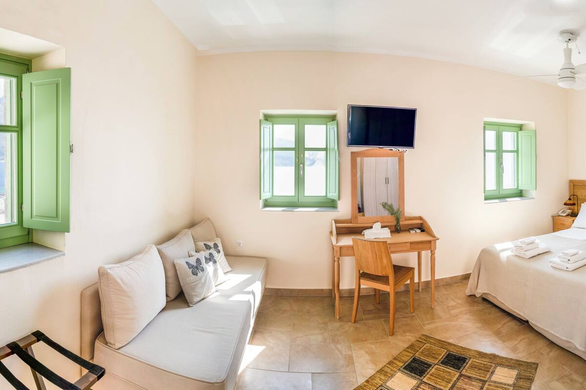 Ein Schlafzimmer mit Bett, Schreibtisch, Stuhl, Fernseher und Fenster.