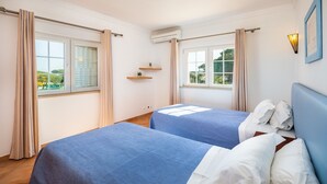 Een hotelkamer met twee bedden, een raam met gordijnen, een wandairconditioning en een klein plankje met een plant.