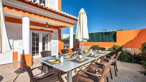 Een terras met een ontbijttafel, rieten stoelen en een grote parasol.