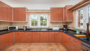 Een keuken met houten kastjes, een magnetron, een waterkoker en een koffiezetapparaat.