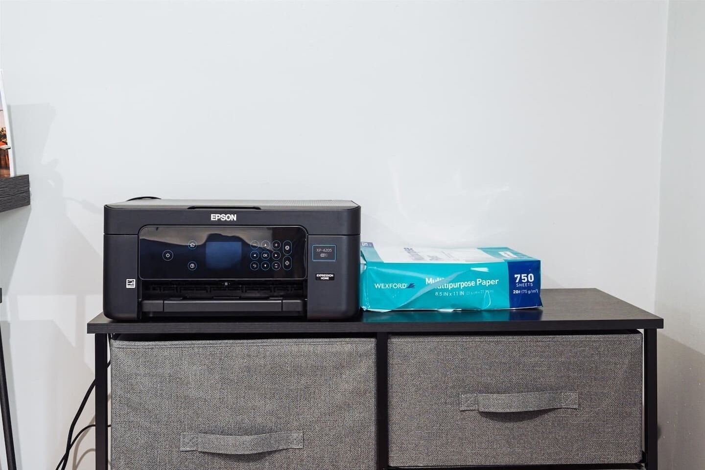 A black Epson printer on a table with a blue box of Wexford multipurpose paper beside it.