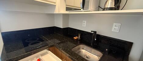 A kitchen with a microwave, coffee maker, sink, and a drawer with utensils.