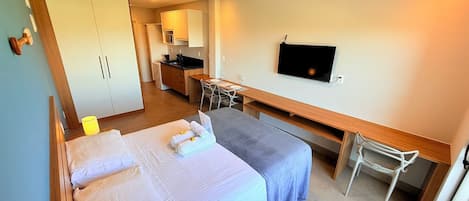 Una habitación de hotel con dos camas, un escritorio, una silla, un televisor y una kitchenette.