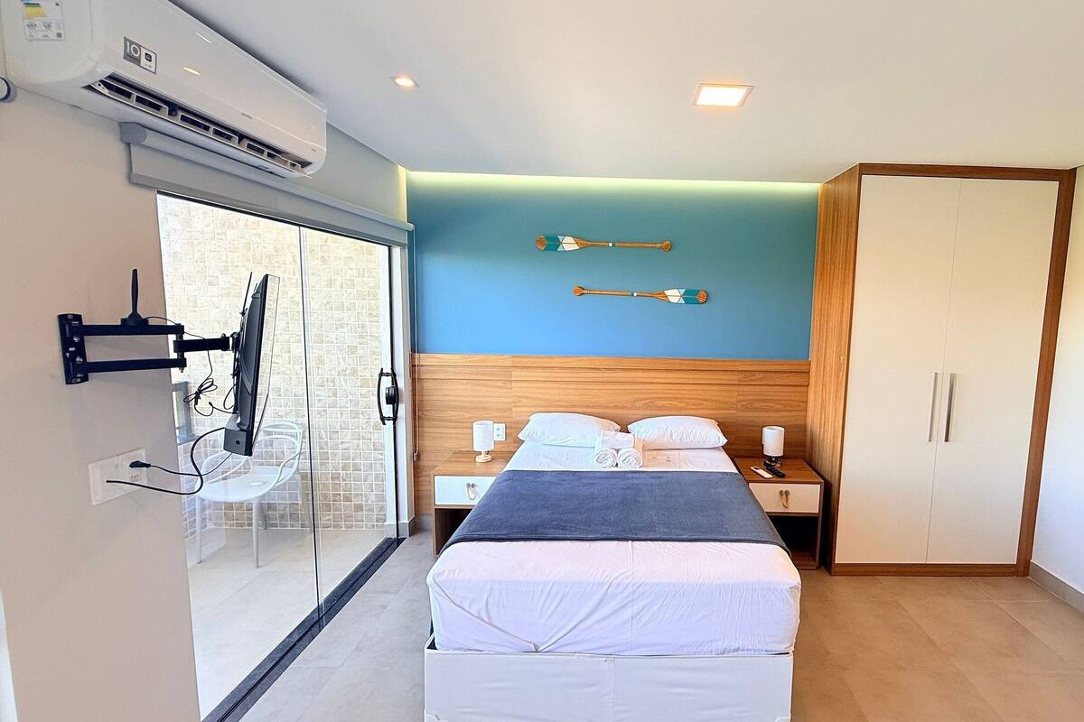 A hotel room with a bed, a wooden headboard, a wardrobe, a TV mounted on the wall, and an air conditioning unit.