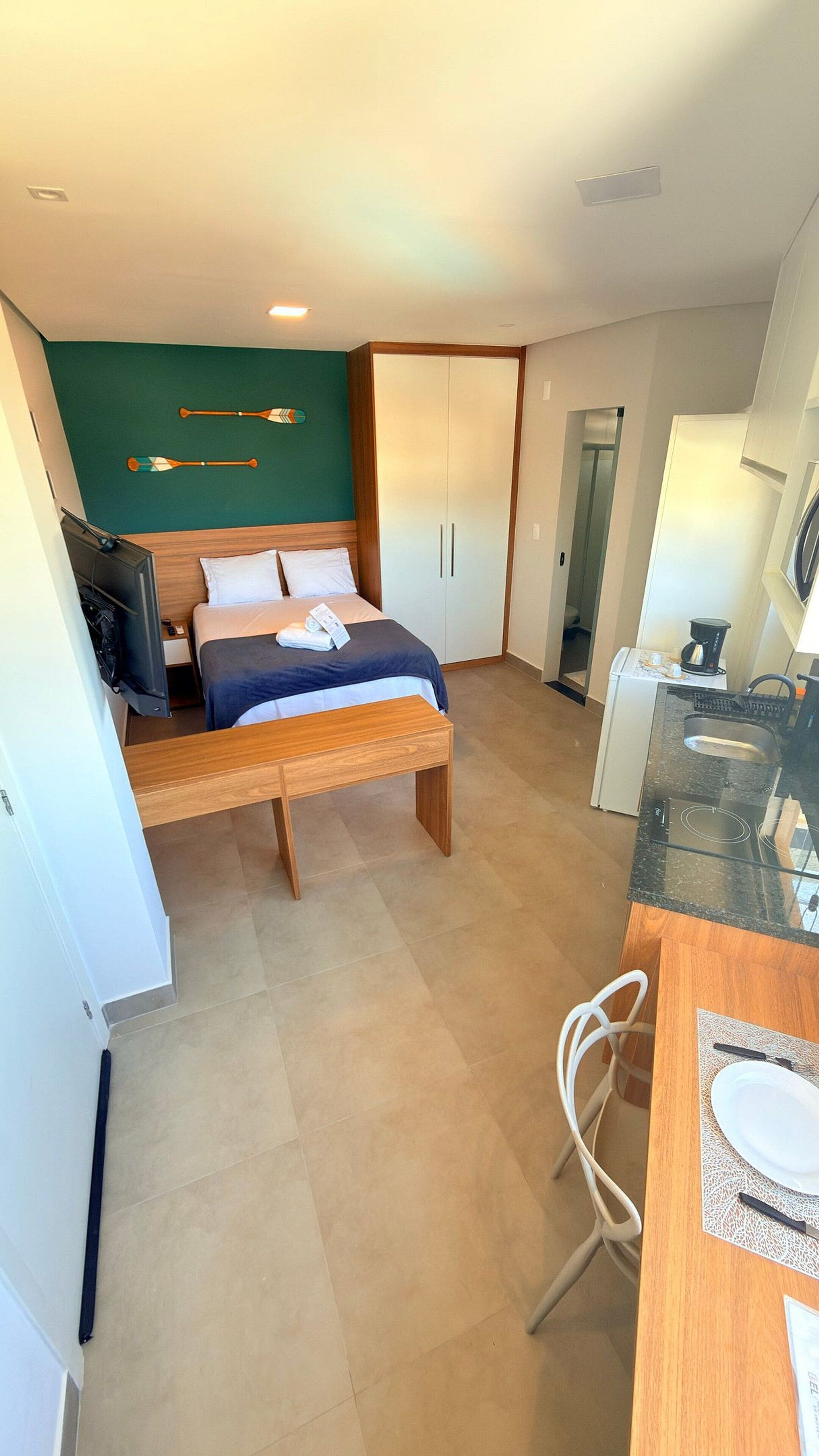 Une chambre d’hôtel de taille réduite, comprenant un lit, un petit bureau, une chaise, une kitchenette et une armoire.