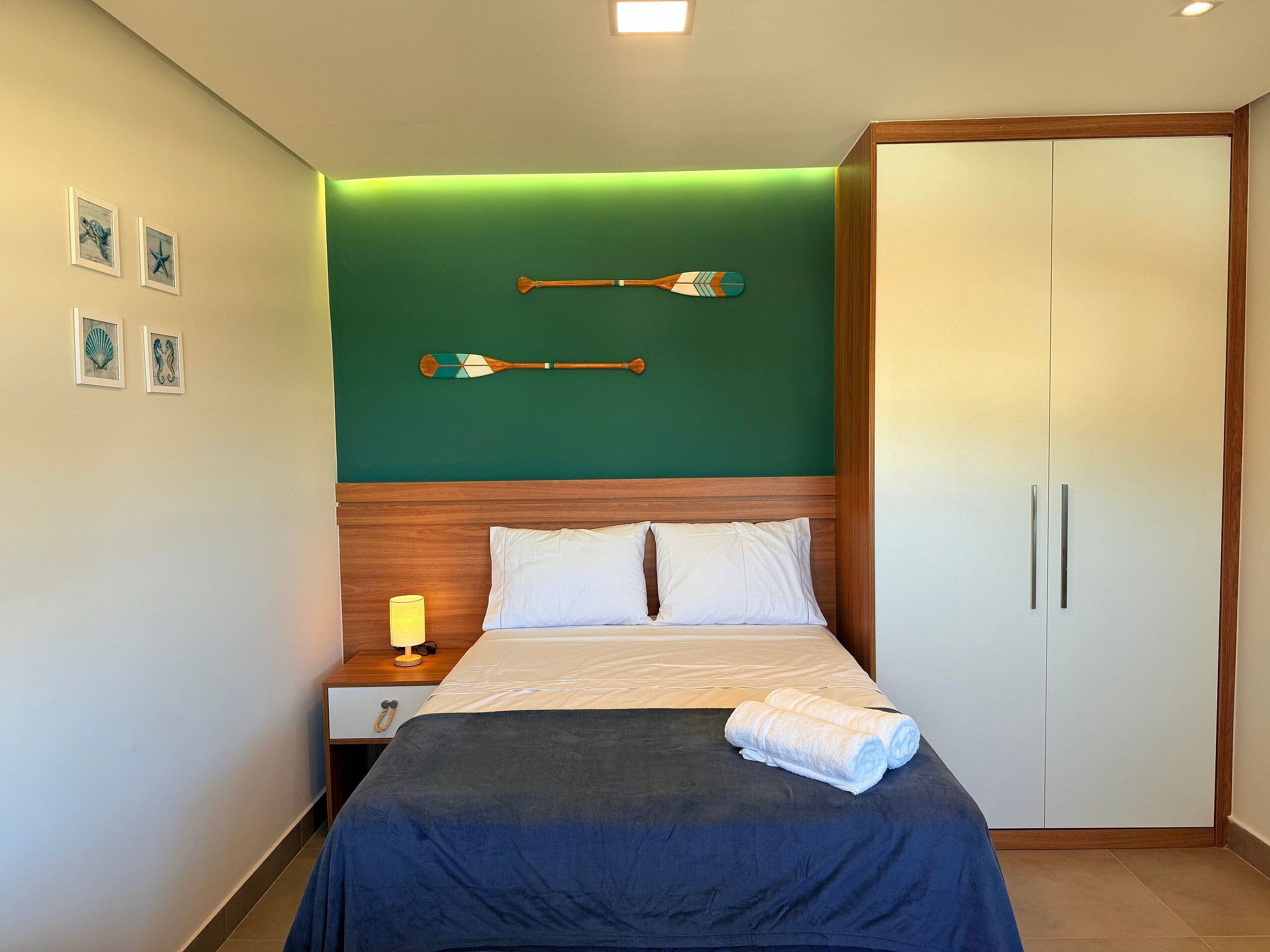 A hotel room with a bed, a nightstand, a lamp, a wardrobe, and wall art.