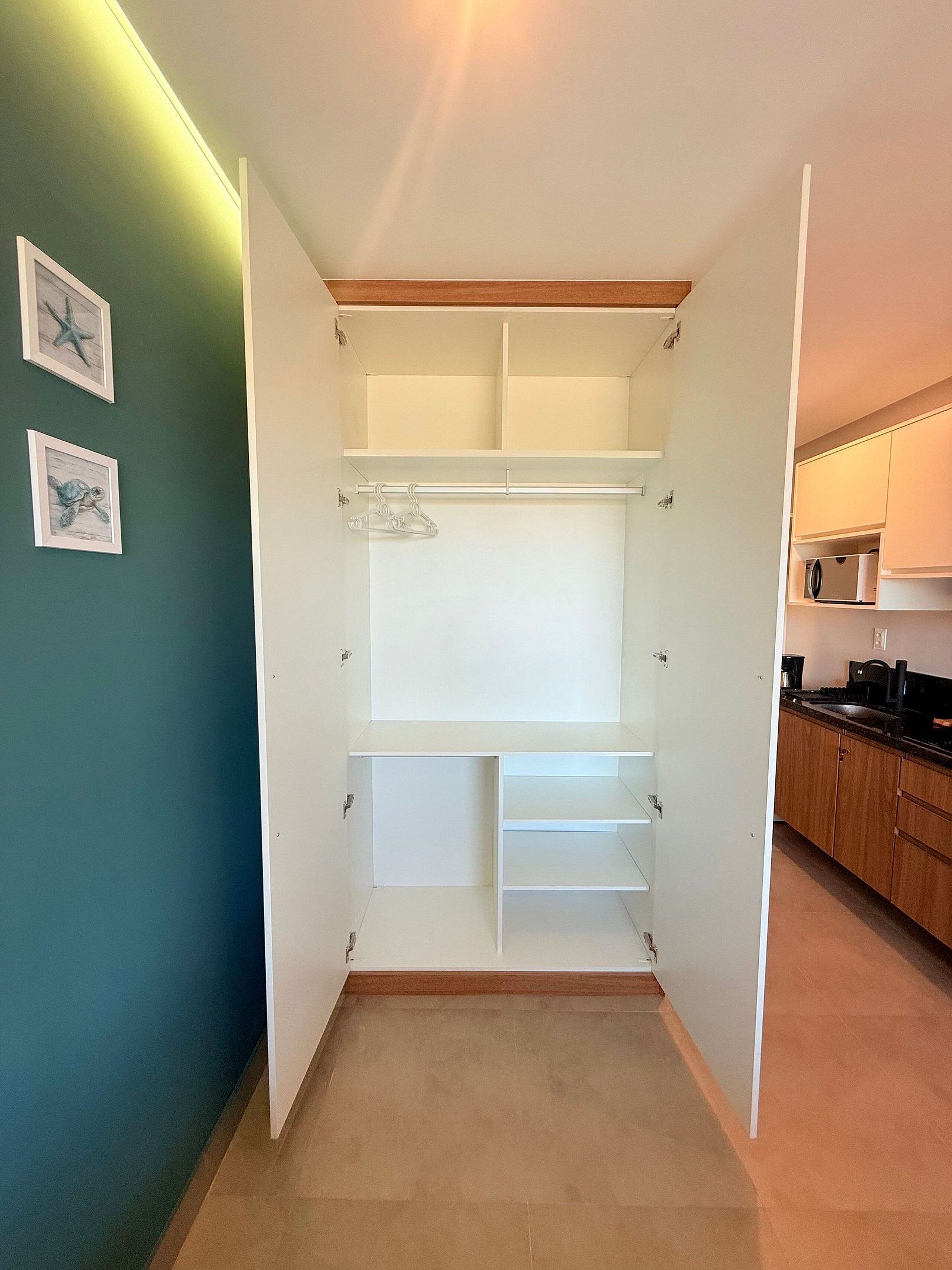Un vestidor amplio con puertas abiertas, piso de madera y una zona de cocina con armarios y electrodomésticos.