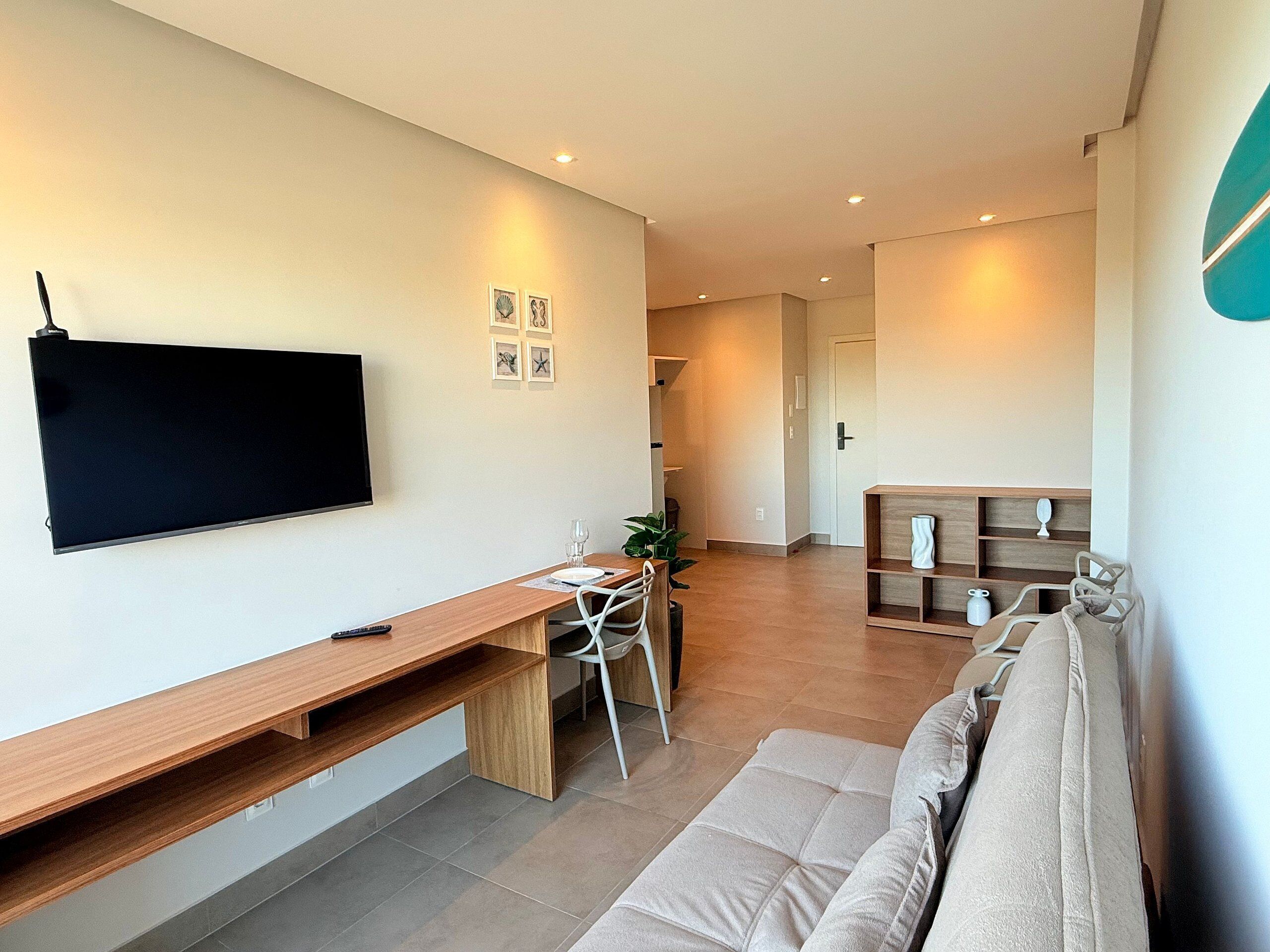 A modern living room with a flat-screen TV, a wooden desk, a sofa, and a bookshelf.