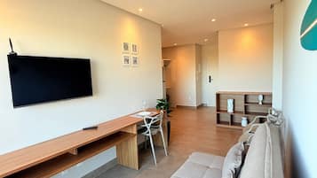 A modern living room with a flat-screen TV, a wooden desk, a sofa, and a bookshelf.