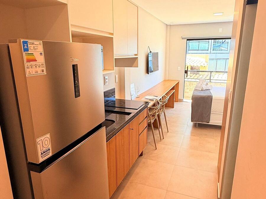 A modern kitchen with a built-in refrigerator, wooden cabinets, a dining area with chairs, and a view through a glass door.
