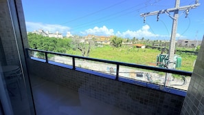 Un balcon donnant sur un champ verdoyant, des bâtiments et des infrastructures électriques.