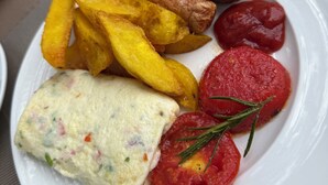 A plate with food items including fries, sausages, a slice of tomato, and a scrambled egg dish.