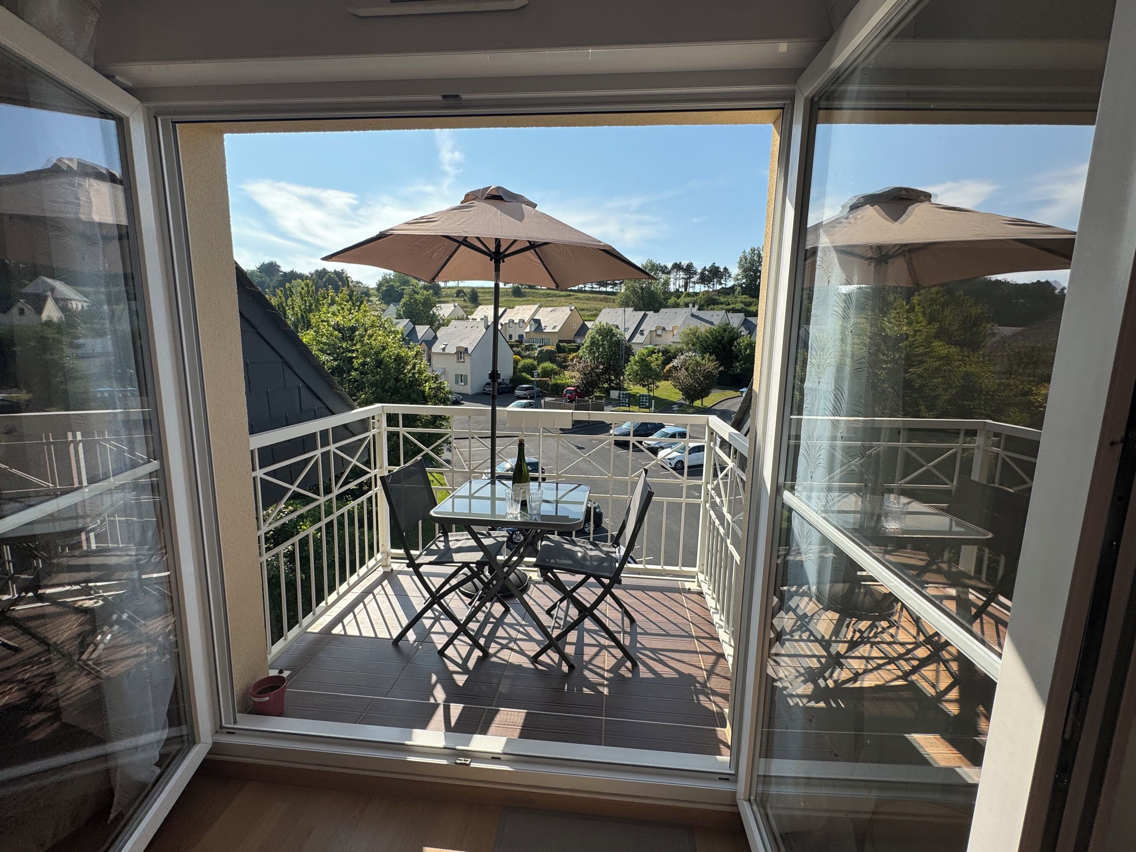 Ein Balkon mit Glastür, Tisch und Stühlen sowie zwei Sonnenschirmen.