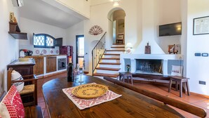 Un amplio salón con una mesa de madera, una escalera, una chimenea y una cocina al fondo.