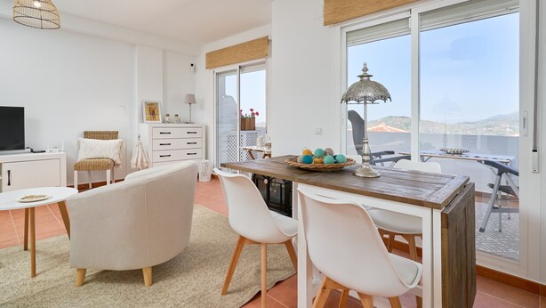 Ein modernes Wohnzimmer mit einer Couch, einem Esstisch, Stühlen, einem Fernseher und einem großen Fenster mit Blick.
