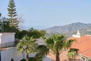 Zona residencial con un edificio blanco, palmeras y vistas a una cadena montañosa.