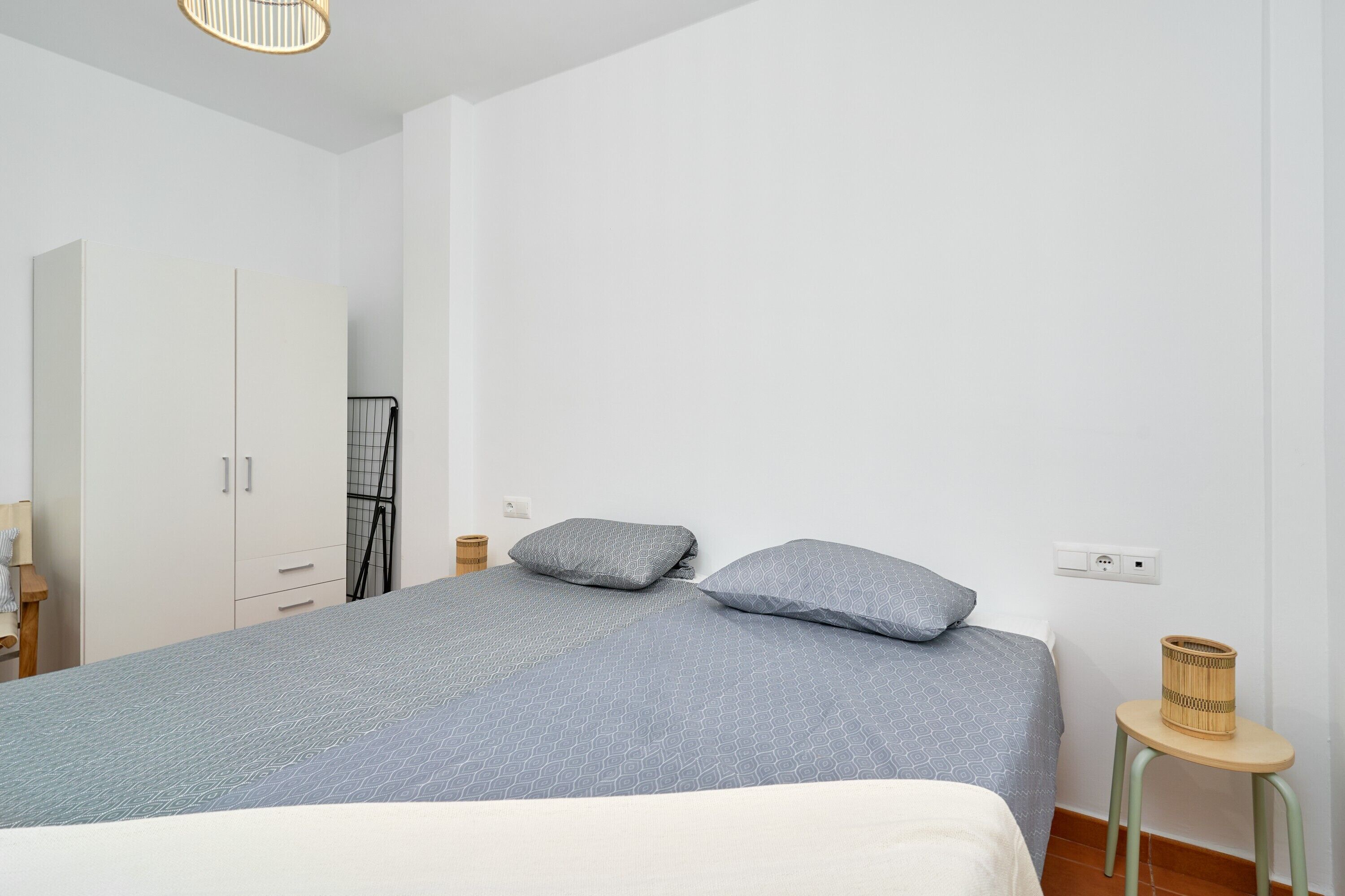 A bedroom with a bed, a wardrobe, a small table, and a lamp.